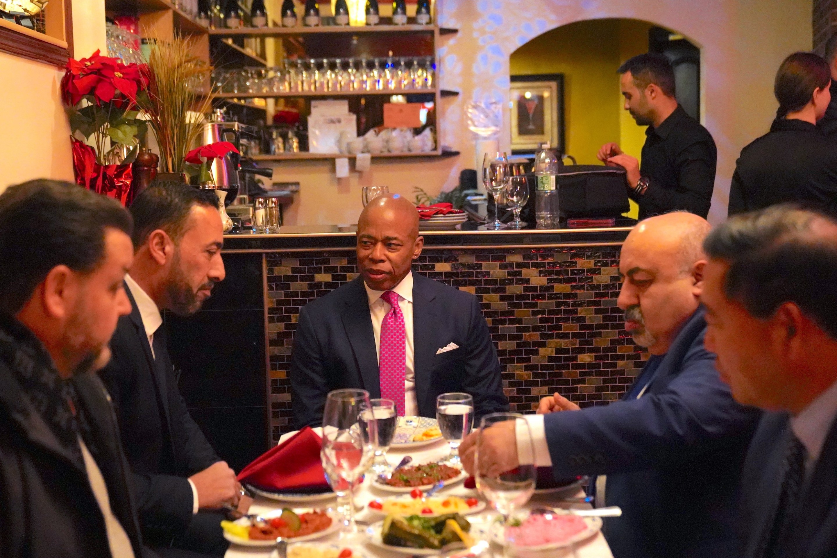 New York City Mayor Eric Adams sitting at a literal table with some restauranteurs at the Manhattan restaurant Ali Baba. This is not the same as the figurative "table of success" at which his haters are his waiters.